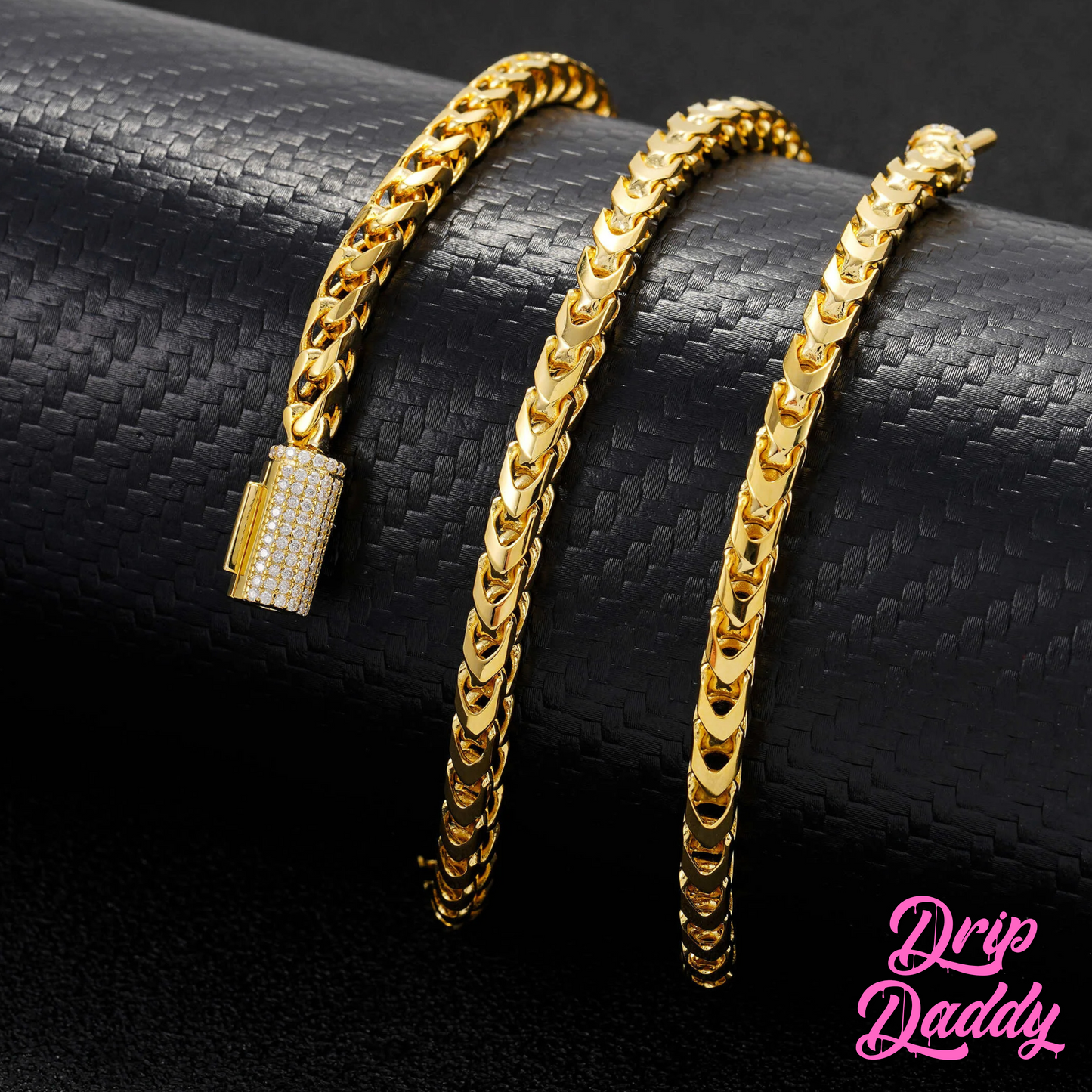 Close-up of Drip Daddy’s Franco Flex 4mm Franco Chain in yellow gold plating with an iced-out moissanite clasp, displayed on a textured black surface, with the pink Drip Daddy logo visible in the bottom right corner.