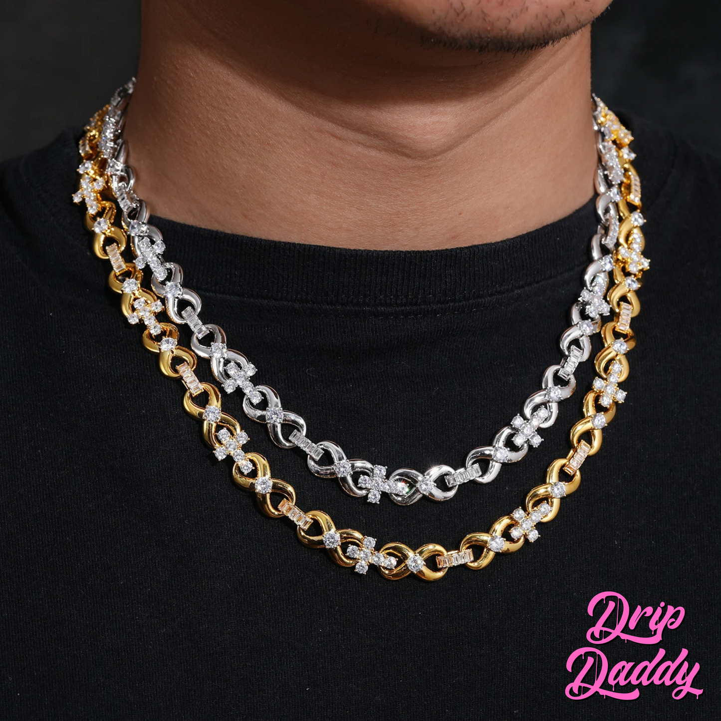 A person wearing two Drip Daddy Infinity Cross Plain – 10mm Mixed Link Chains, one in white gold and one in yellow gold plating, styled over a black shirt. The Drip Daddy logo is placed in pink at the bottom right.