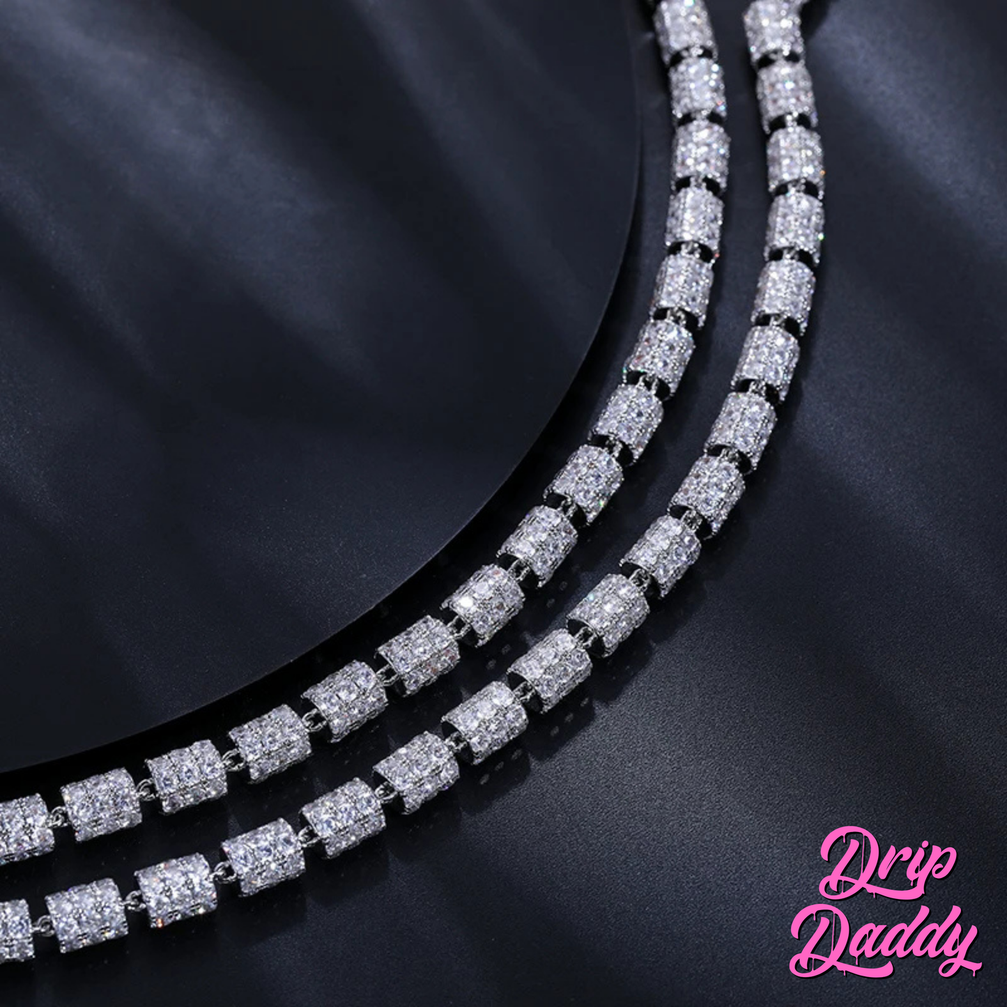 Close-up of Drip Daddy’s Stargazer Cylinder – 7mm Moissanite Chain in white and yellow gold plating, showing two rows of detailed iced cylinder links against a dark reflective surface, with the Drip Daddy logo visible in pink at the bottom right corner.