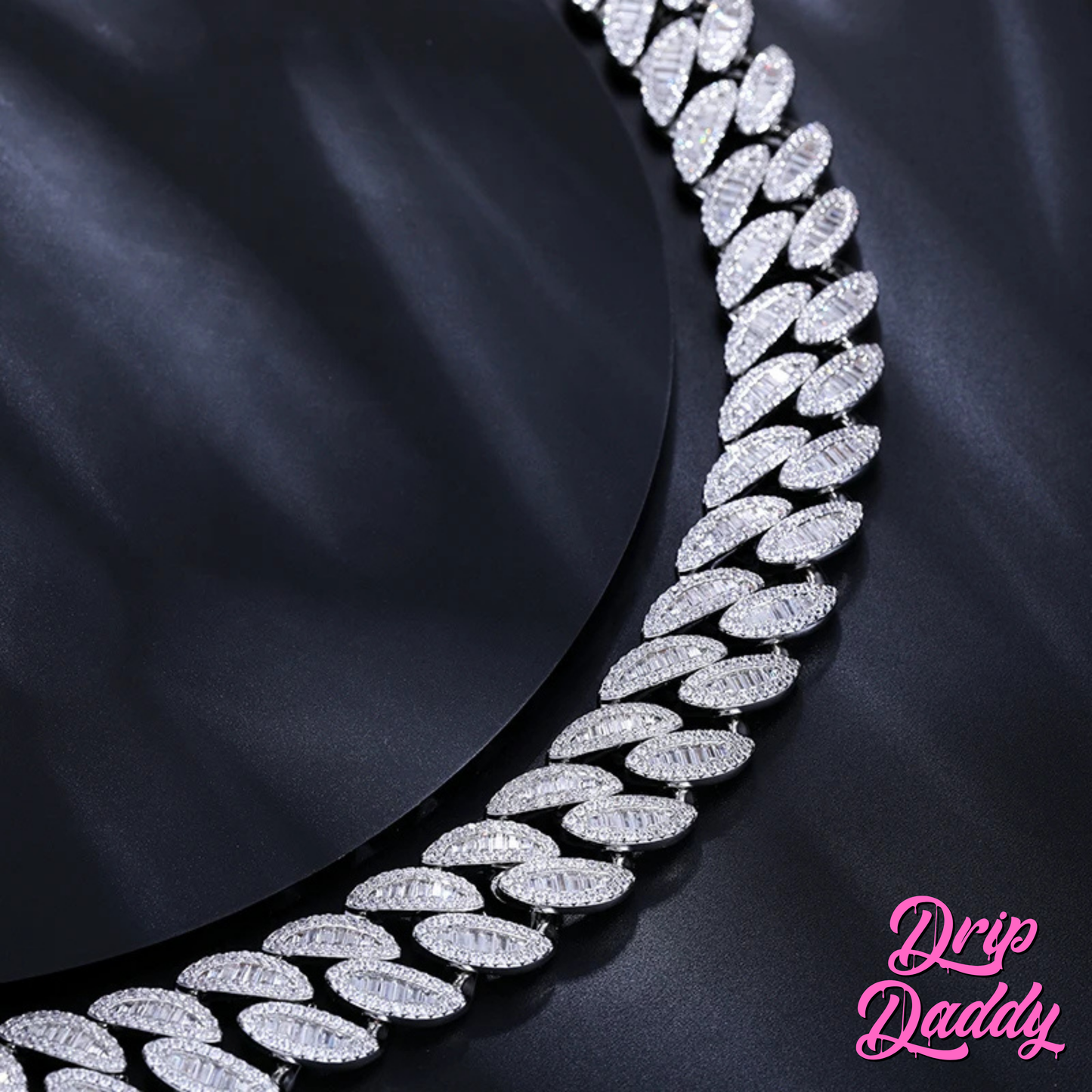 Close-up of Drip Daddy’s The Enforcer 20mm Mixed-Cut Cuban Link Chain in white gold with diamond detailing, displayed flat on a dark fabric background with the Drip Daddy logo in pink at the bottom right corner.