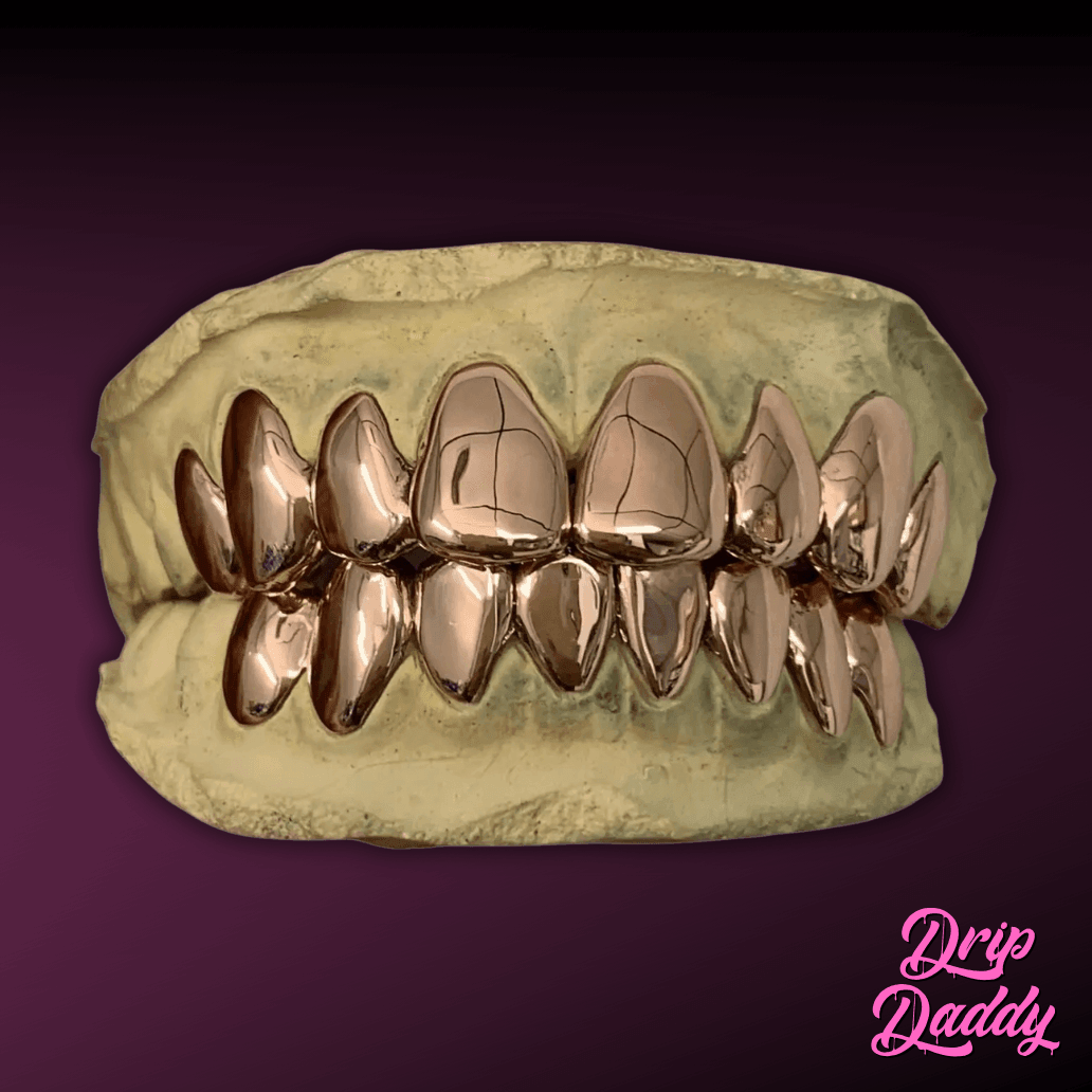 A stone dental mold exhibits Solid Plain Grillz crafted in yellow gold, covering both upper and lower teeth. The reflective finish is set against a maroon-to-purple gradient, with the Drip Daddy logo in pink cursive at the bottom right.