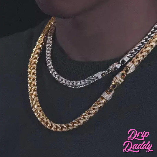 A person wears two thick Moissanite Franco Chains—one yellow gold plated, one white gold plated—over a black shirt. Both have decorative clasps. The Drip Daddy logo appears in pink at the bottom right.