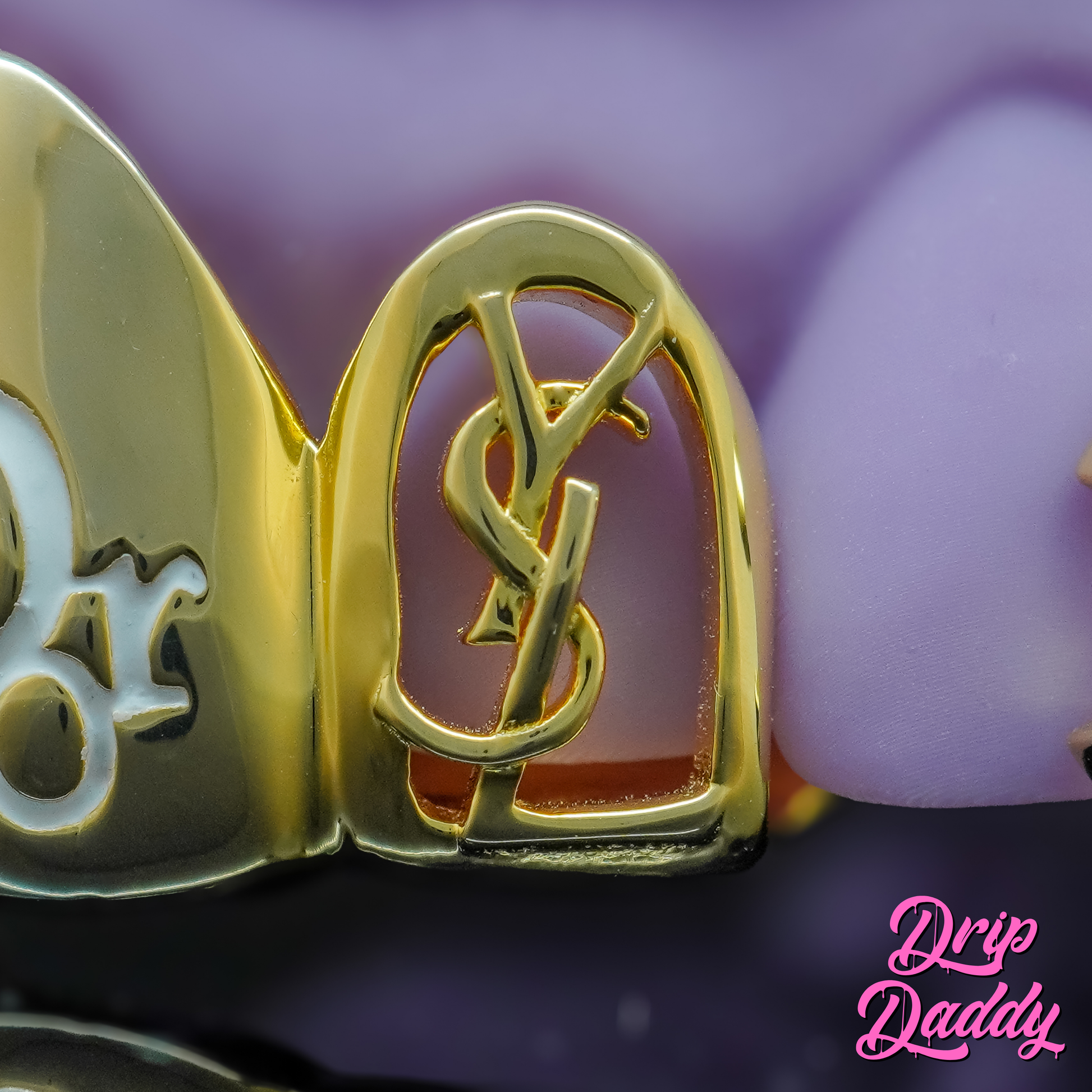 Custom gold grillz featuring a YSL-inspired cut-out logo object design on a tooth cap by Drip Daddy.