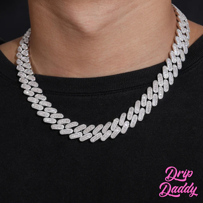 A person wearing Drip Daddy’s Capsule – Mixed-Cut Cuban Chain in 14mm white gold plating over a black shirt. The diamond-encrusted design sparkles under lighting, with the Drip Daddy logo in pink at the bottom right.