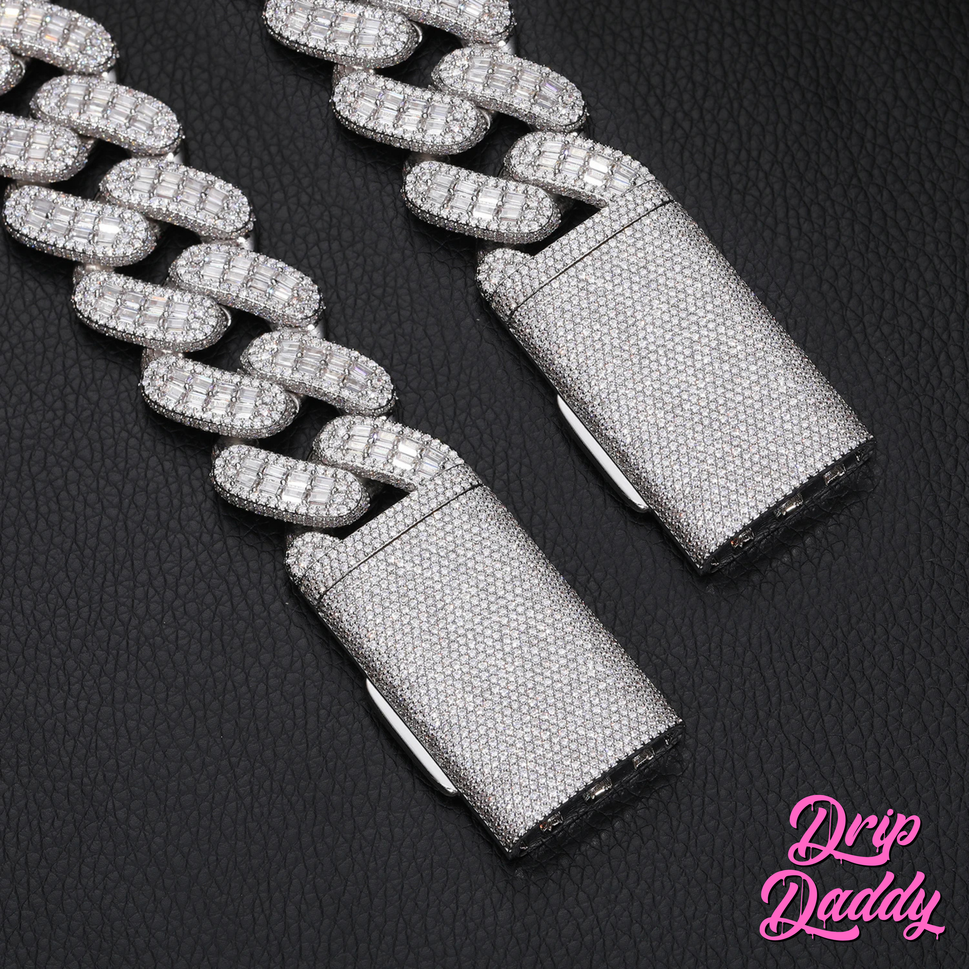 Close-up of Drip Daddy’s Capsule – Mixed-Cut Cuban Chain in 28mm white gold plating, highlighting the diamond-encrusted clasp against a black textured background. The Drip Daddy logo is visible in pink at the bottom right.