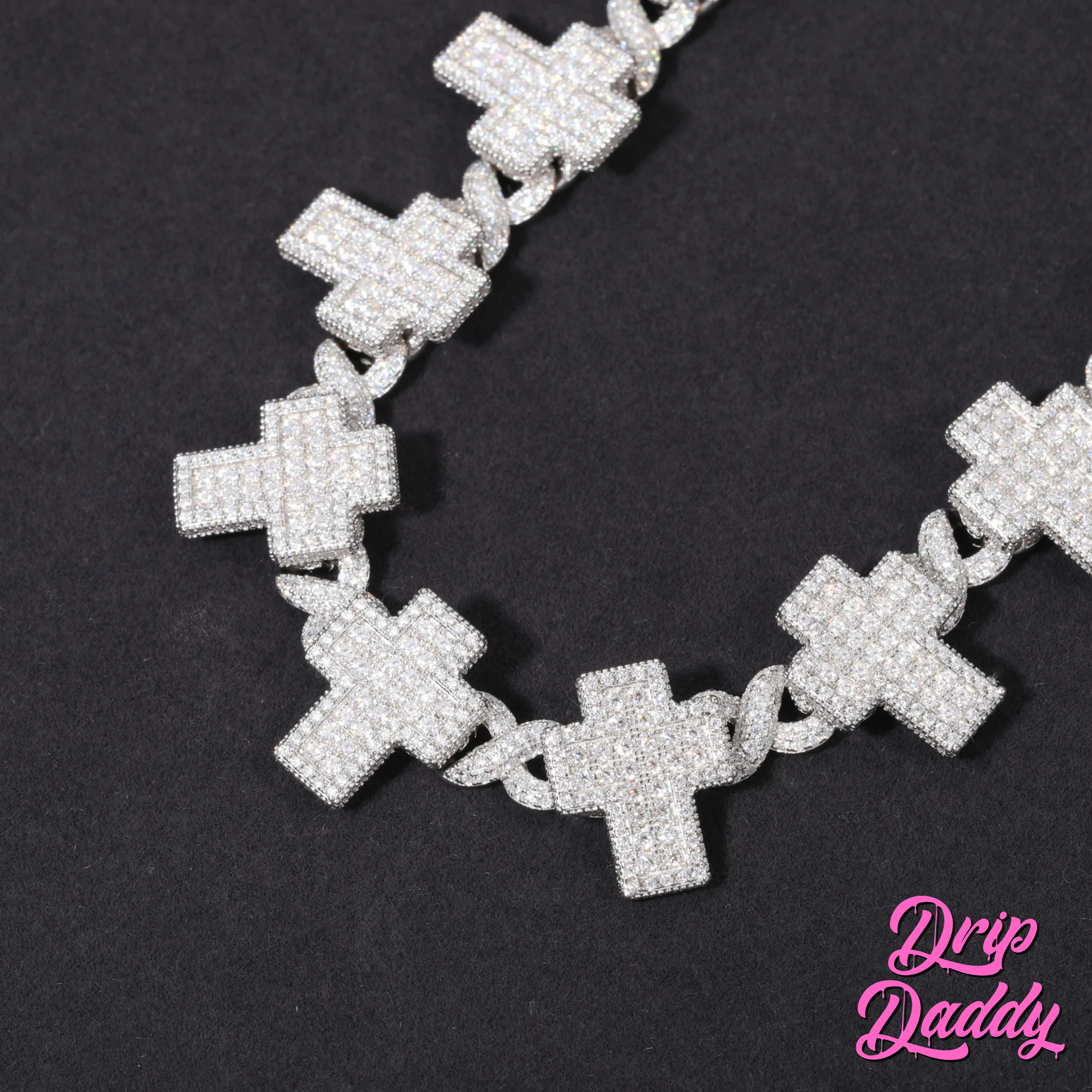 Close-up of Drip Daddy’s Crucifix Link – 8mm Moissanite Chain in white gold plating, focusing on the detailed iced crucifix links connected by moissanite-studded Cuban-style links against a black background, with the pink Drip Daddy logo in the bottom right corner.