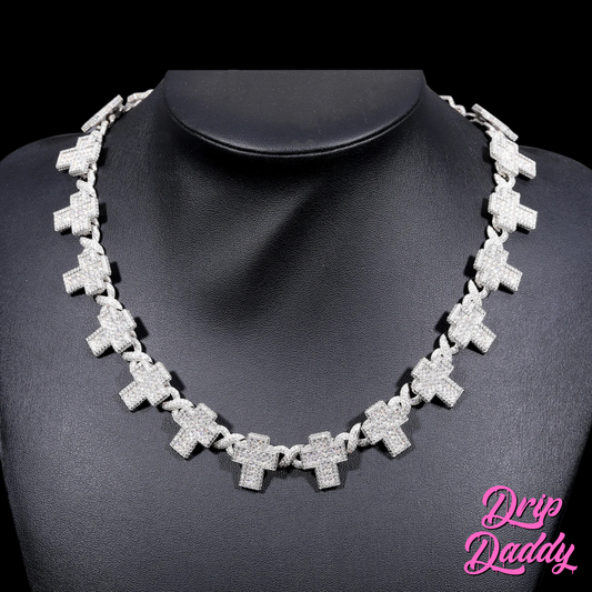 A person wearing Drip Daddy’s Crucifix Link – 8mm Moissanite Chain in white gold plating, styled on a mannequin bust to showcase the full chain of iced crucifix links, with the pink Drip Daddy logo in the bottom right corner.