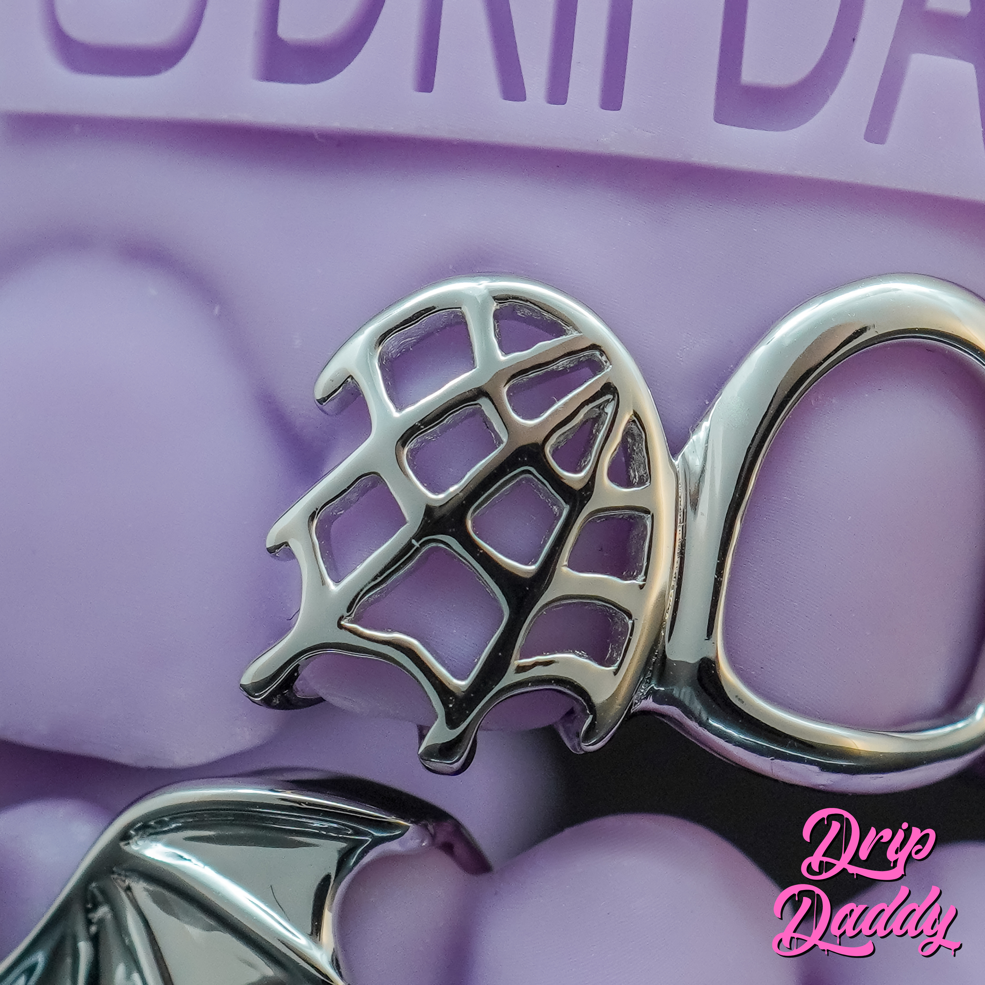 Close-up of Drip Daddy Cut-Out Grillz in sterling silver with a spiderweb design, displayed on a textured purple background with the Drip Daddy watermark.