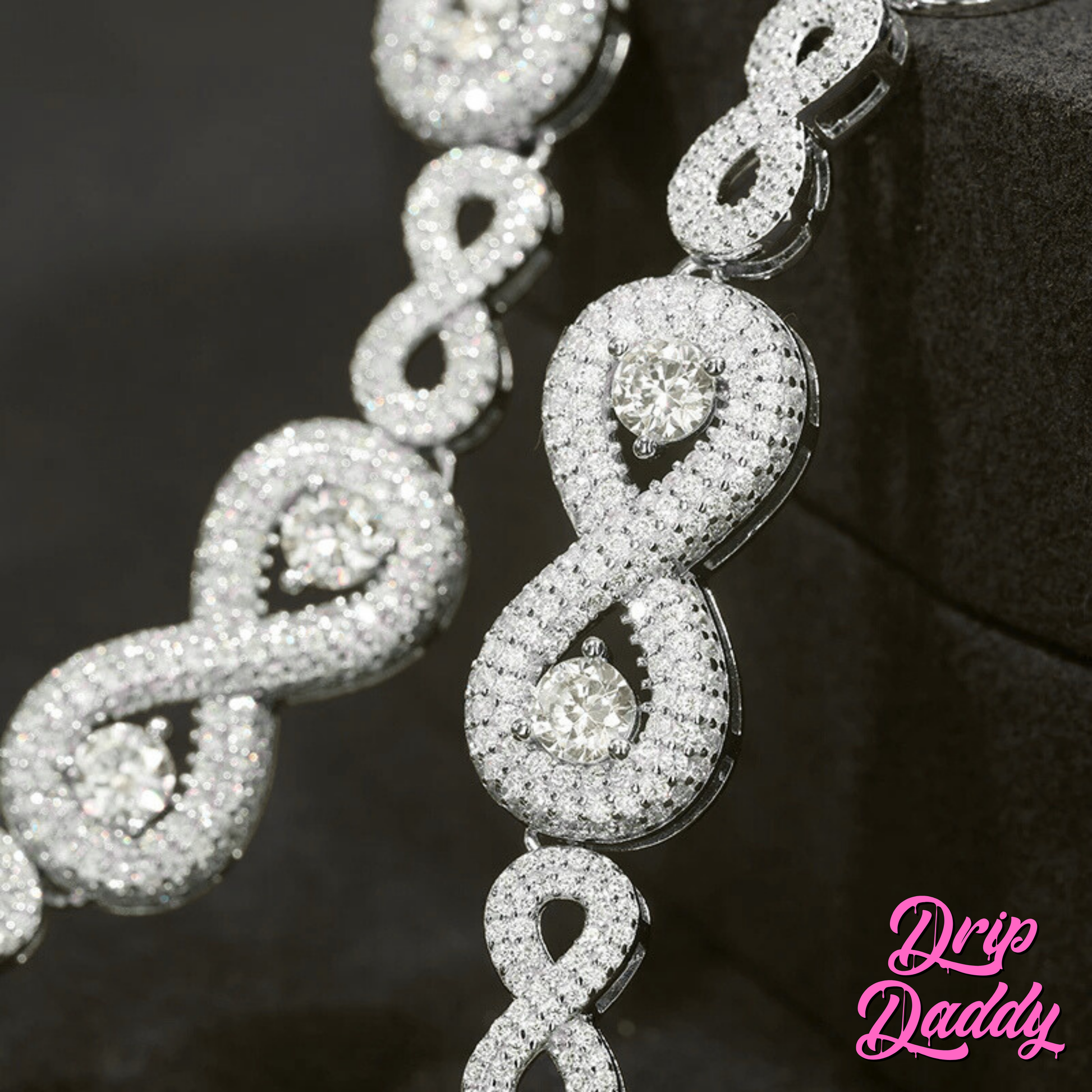 Close-up of Drip Daddy’s Eternal Drip – 12mm Moissanite Chain in white and yellow gold plating draped vertically to highlight the interlocking infinity-style links and round-cut center stones, with the Drip Daddy logo in pink visible in the bottom right corner.