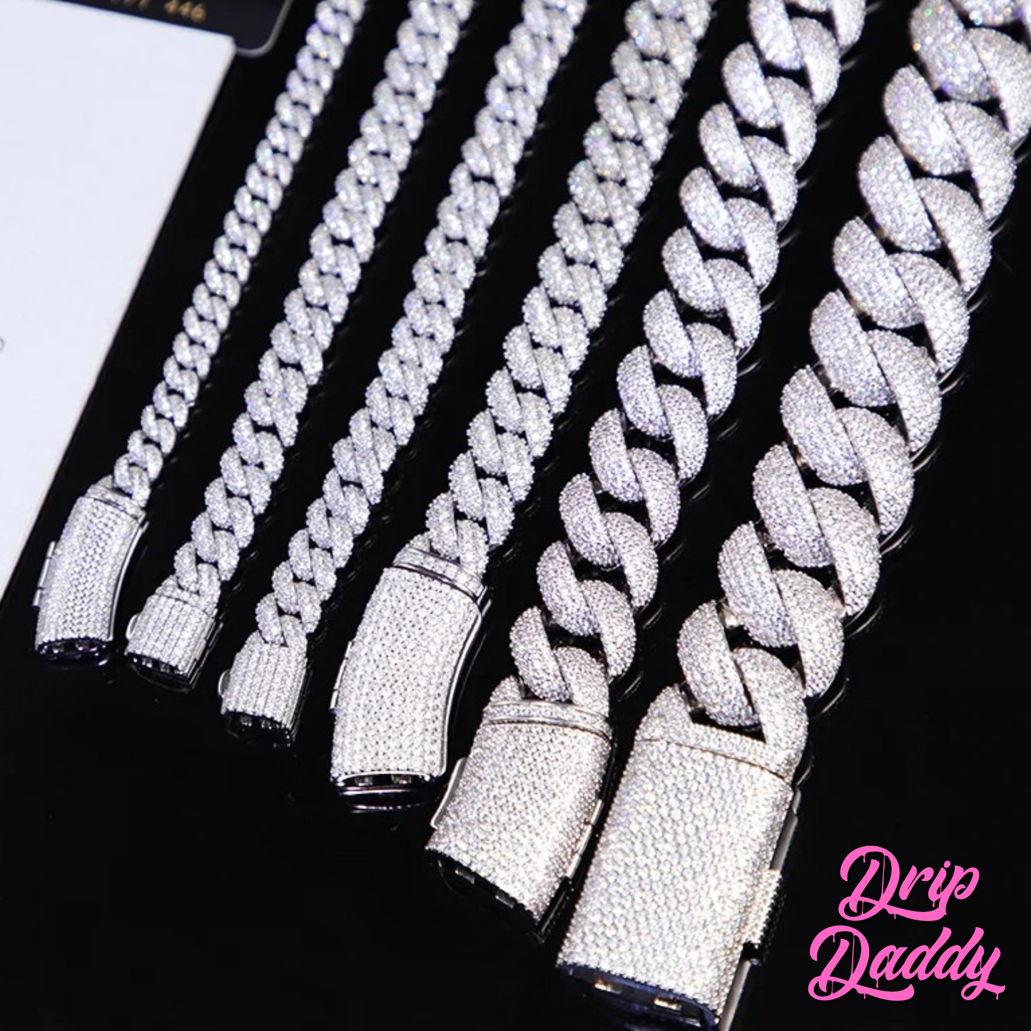A person wearing Drip Daddy’s Frosted Miami Cuban Link Chain in 12mm, crafted in white gold plating with moissanite stones, layered in multiple lengths over a black shirt, with the Drip Daddy logo in pink at the bottom right.