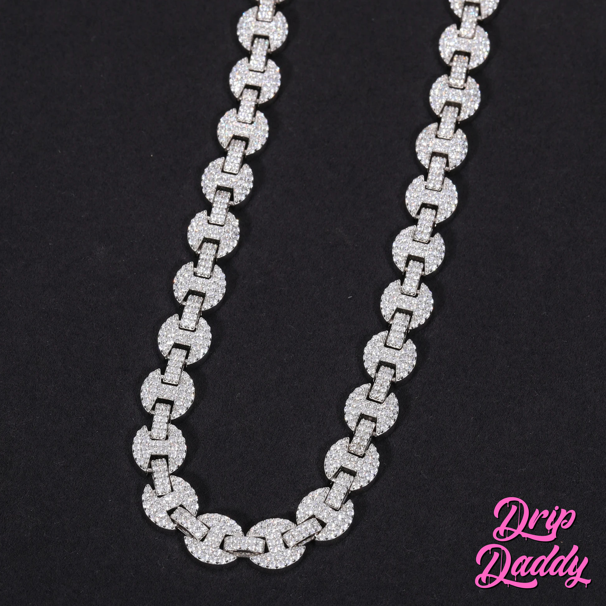Close-up of Drip Daddy’s Gemlock Link chain in 6mm to 10mm size, crafted in white gold plating with moissanite stones, laid flat on a black surface with the Drip Daddy logo in pink at the bottom right.
