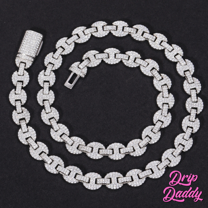 Close-up of Drip Daddy’s Gemlock Link chain in 6mm to 10mm size, crafted in white gold plating with moissanite stones, displayed coiled on a black surface with the Drip Daddy logo in pink at the bottom right.