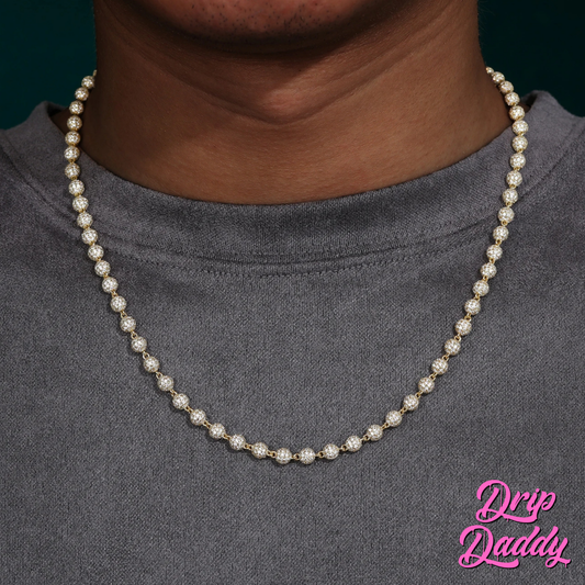 A person wearing Drip Daddy’s Ice Orbit 5mm to 10mm moissanite chain in yellow gold plated finish, styled over a grey crewneck shirt, with the Drip Daddy logo in pink at the bottom right corner.