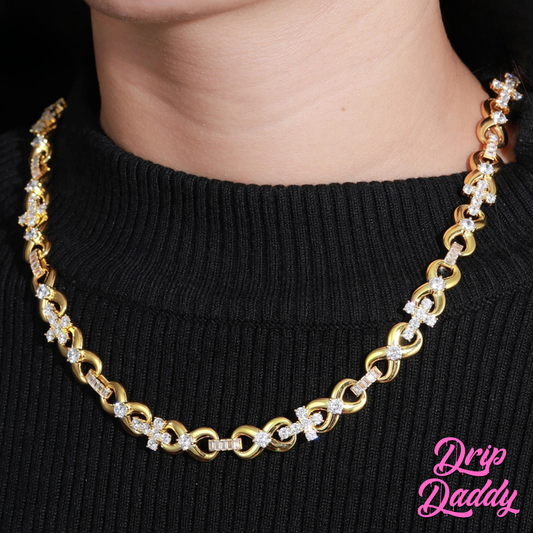 A person wearing Drip Daddy’s Infinity Cross Plain – 10mm Mixed Link Chain in yellow gold plating, styled over a black sweater. The Drip Daddy logo is visible in pink at the bottom right.