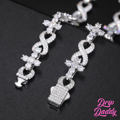Close-up of Drip Daddy’s Infinity Link bracelet in white gold with iced-out moissanite stones, laid on a black background with the pink Drip Daddy logo visible in the corner.