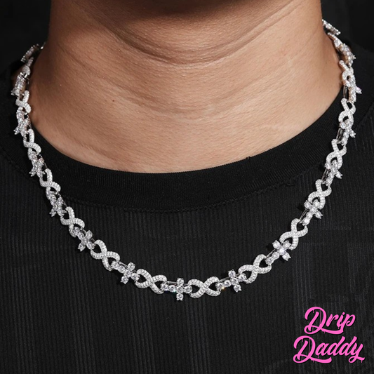 A person wearing Drip Daddy’s Infinity Link necklace in white gold with iced-out moissanite stones, photographed at an angled view over a black shirt, with the pink Drip Daddy logo visible in the corner.