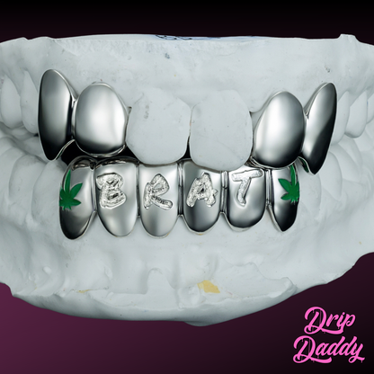 Custom silver engraved letter grillz by Drip Daddy spelling “BRAT” across four teeth, featuring engraved cannabis leaf designs on each side. Shown on a white dental mold against a purple background with Drip Daddy logo.