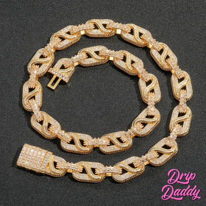 The Snowdrift – 14mm Baguette & Round Moissanite Link Chain in yellow gold plating by Drip Daddy, iced-out and coiled flat on a black surface with the Drip Daddy logo in pink.