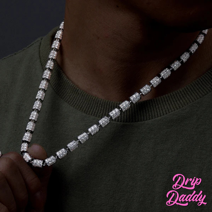 A person wearing Drip Daddy’s Stargazer Cylinder – 7mm Moissanite Chain in white and yellow gold plating, shown being held up across the chest, with the Drip Daddy logo visible in pink at the bottom right corner.