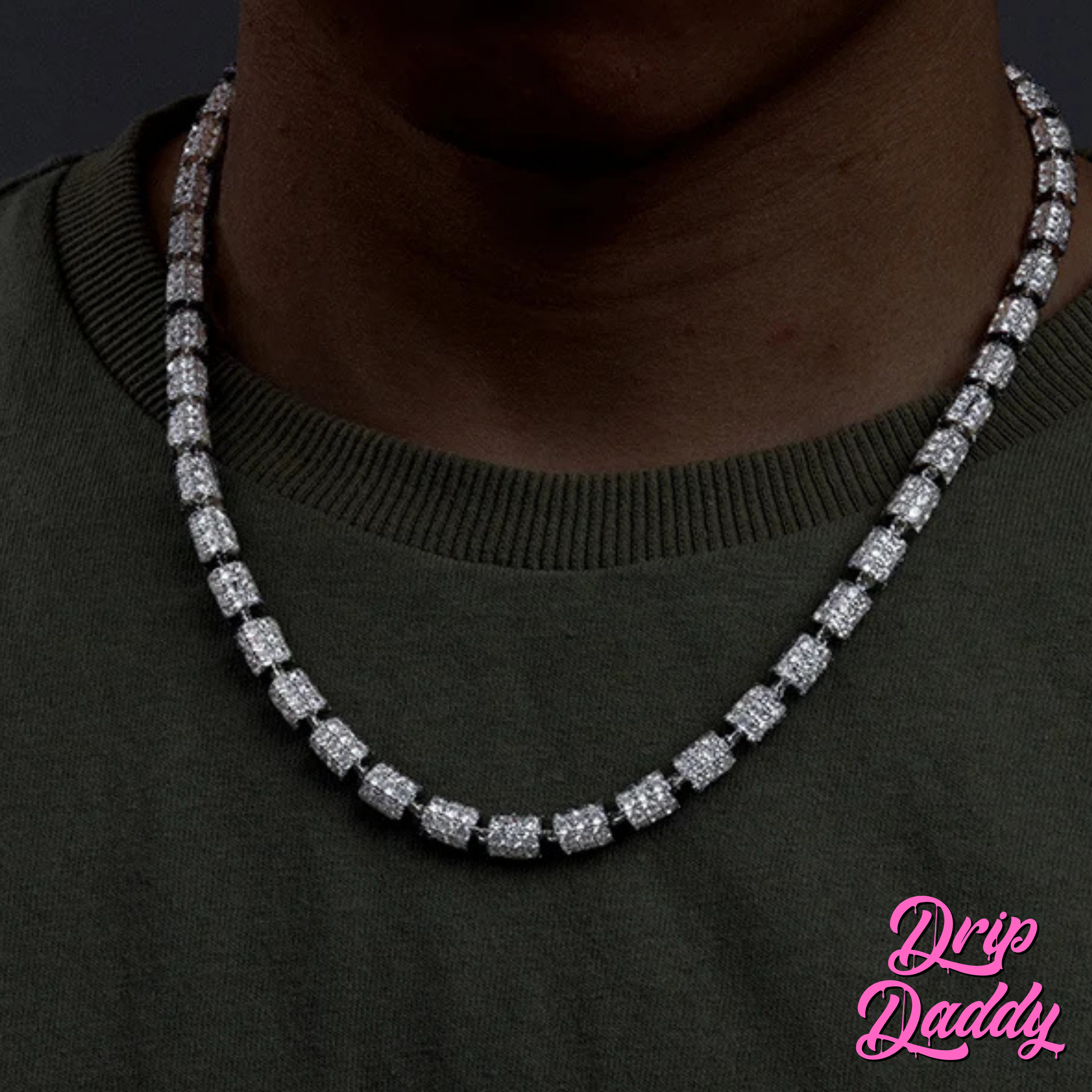A person wearing Drip Daddy’s Stargazer Cylinder – 7mm Moissanite Chain in white and yellow gold plating, styled around the neck with an olive green shirt, with the Drip Daddy logo visible in pink at the bottom right corner.