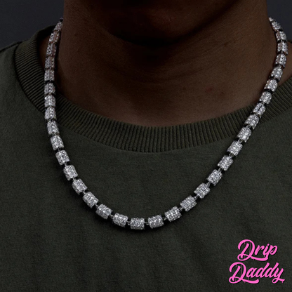 A person wearing Drip Daddy’s Stargazer Cylinder – 7mm Moissanite Chain in white and yellow gold plating, styled around the neck with an olive green shirt, with the Drip Daddy logo visible in pink at the bottom right corner.