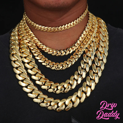 A person wearing Drip Daddy’s The Don – 20mm to 30mm Miami Cuban Link Chain in a yellow gold plated finish, styled in multiple layered lengths on a black shirt, with the Drip Daddy logo in pink visible in the bottom right corner.