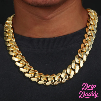 A person wearing Drip Daddy’s The Don – 20mm to 30mm Miami Cuban Link Chain in a yellow gold plated finish, shown as a single chain around the neck on a black shirt, with the Drip Daddy logo in pink visible in the bottom right corner.