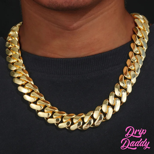 A person wearing Drip Daddy’s The Don – 20mm to 30mm Miami Cuban Link Chain in a yellow gold plated finish, shown as a single chain around the neck on a black shirt, with the Drip Daddy logo in pink visible in the bottom right corner.