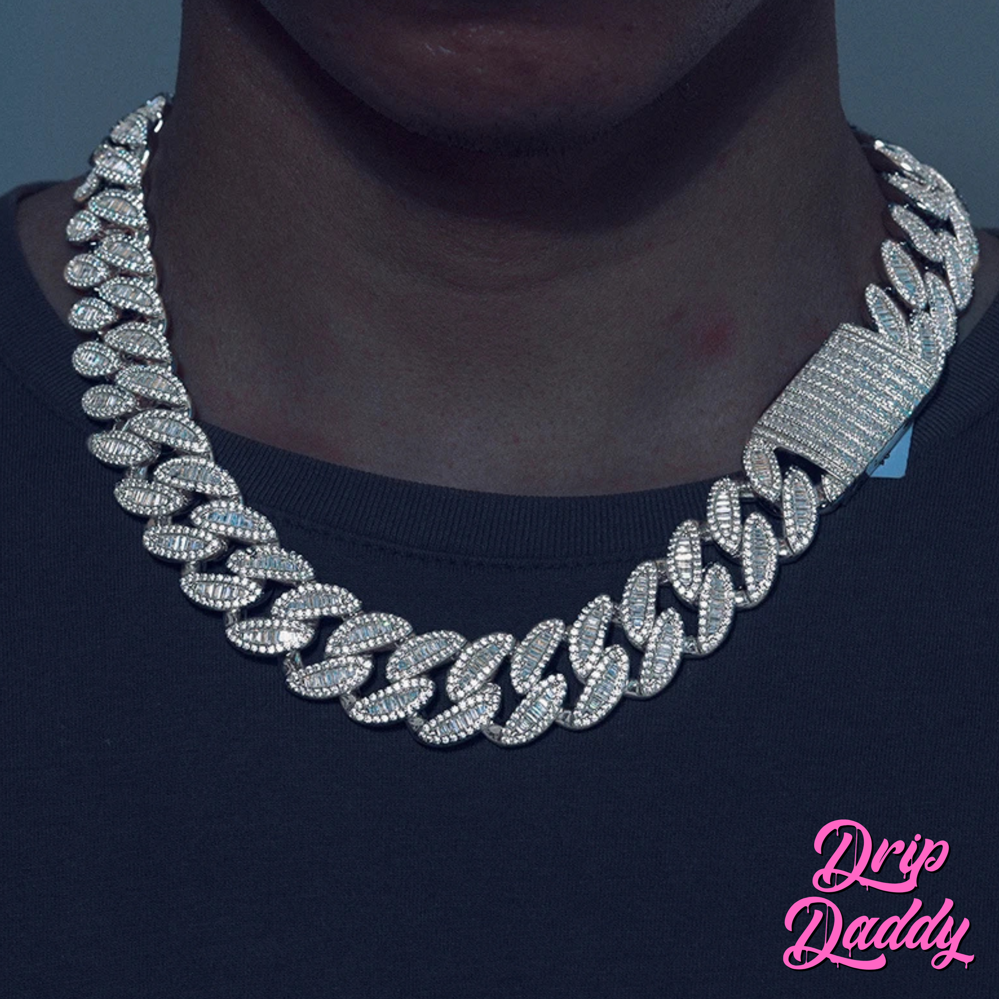 A person wearing Drip Daddy’s The Enforcer 20mm Mixed-Cut Cuban Link Chain in white gold with diamond detailing, shown against a dark shirt background with the Drip Daddy logo in pink at the bottom right corner.