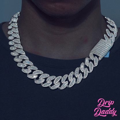 A person wearing Drip Daddy’s The Enforcer 20mm Mixed-Cut Cuban Link Chain in white gold with diamond detailing, shown against a dark shirt background with the Drip Daddy logo in pink at the bottom right corner.