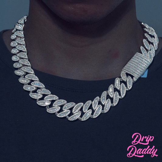 A person wearing Drip Daddy’s The Enforcer 20mm Mixed-Cut Cuban Link Chain in white gold with diamond detailing, shown against a dark shirt background with the Drip Daddy logo in pink at the bottom right corner.