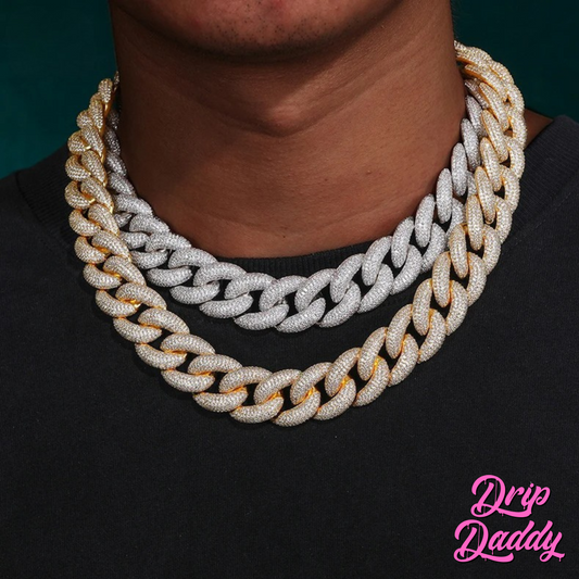 A person wearing two of Drip Daddy’s The Heavy Hitter 20mm to 30mm Moissanite Miami Cuban Link Chains layered together, one in white gold plated finish and the other in yellow gold plated finish, styled over a black shirt, with the Drip Daddy logo in pink in the bottom right corner.