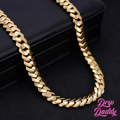 Close-up of Drip Daddy’s The Hustler Cuban Link Chain in yellow gold plated finish displayed on a black leather case, with the pink Drip Daddy logo visible in the bottom right corner.