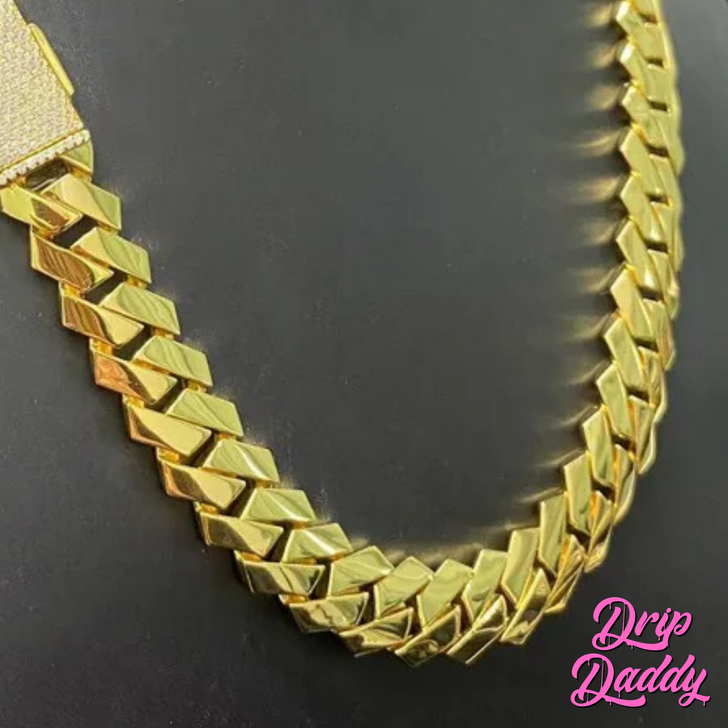 Close-up of Drip Daddy’s The Hustler Cuban Link Chain in yellow gold plated finish on a dark surface, showcasing the bold interlocking links and iced clasp detail, with the pink Drip Daddy logo visible in the bottom right corner.