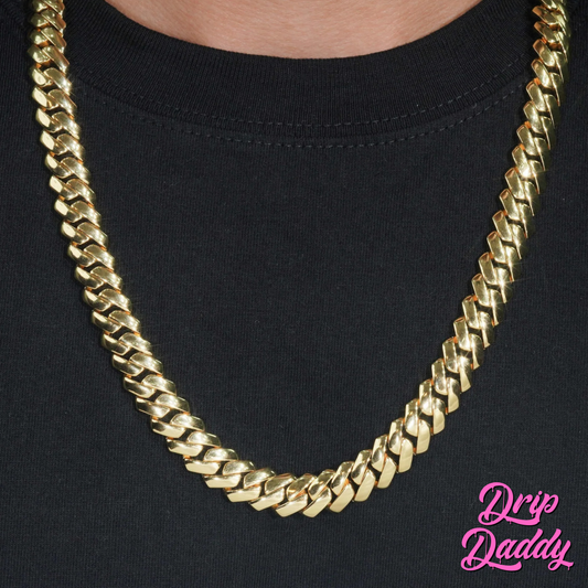 A person wearing Drip Daddy’s The Hustler Cuban Link Chain in yellow gold plated finish over a plain black t-shirt, with the pink Drip Daddy logo visible in the bottom right corner.