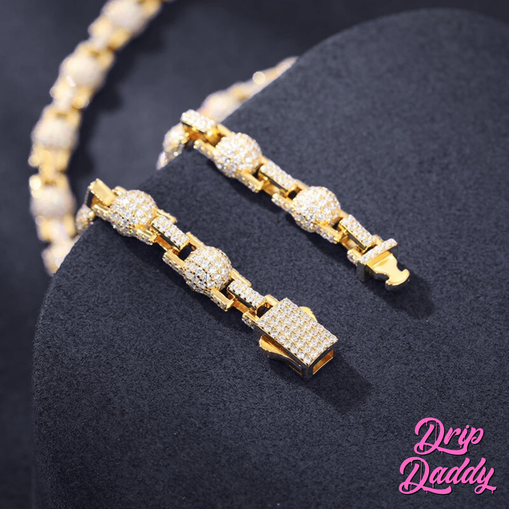 Close-up of Drip Daddy’s The Juggernaut – 7mm Moissanite Bead Link Chain in yellow gold plating, displayed on a dark stand with detailed focus on the clasp and links, with the Drip Daddy logo in pink at the bottom right.