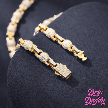 Close-up of Drip Daddy’s The Juggernaut – 7mm Moissanite Bead Link Chain in yellow gold plating, displayed on a dark stand with detailed focus on the clasp and links, with the Drip Daddy logo in pink at the bottom right.