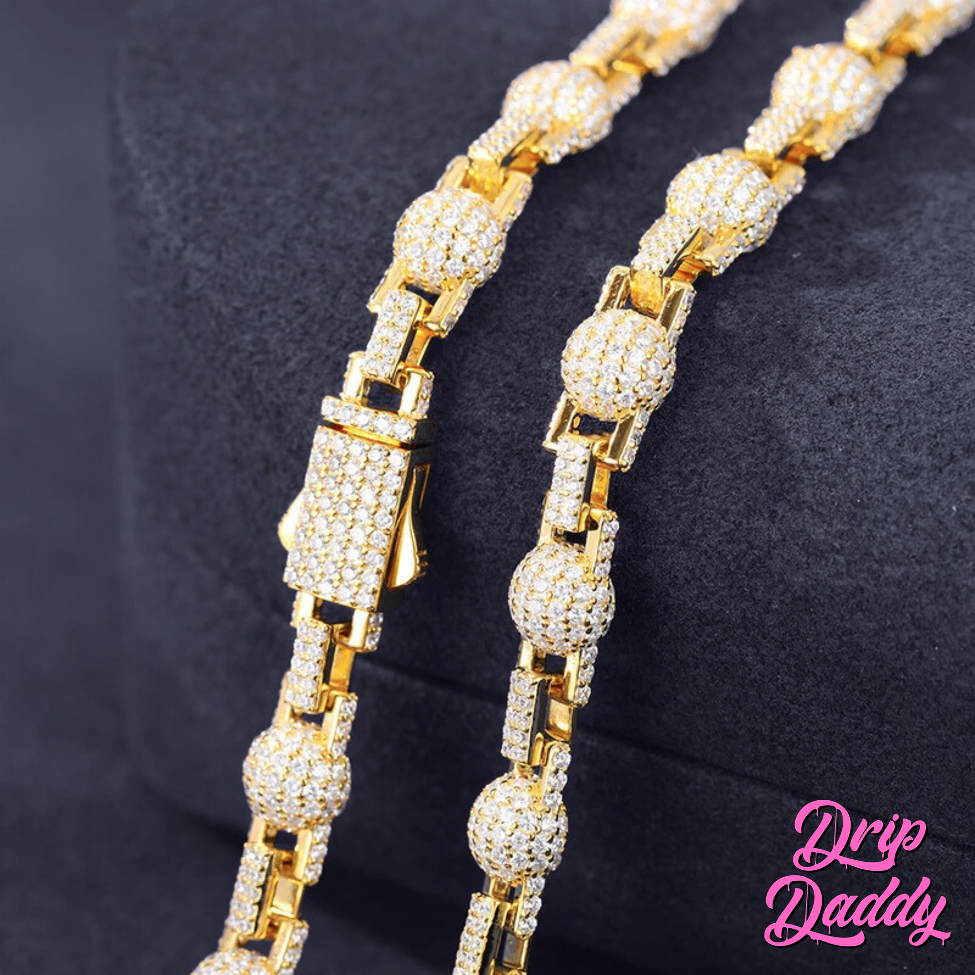 Close-up of Drip Daddy’s The Juggernaut – 7mm Moissanite Bead Link Chain in yellow gold plating, showing two parallel sections of the chain with detailed moissanite settings on a dark background, with the Drip Daddy logo in pink at the bottom right.