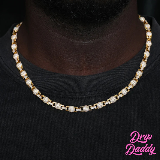 A person wearing Drip Daddy’s The Juggernaut – 7mm Moissanite Bead Link Chain in yellow gold plating, styled over a black shirt, with the Drip Daddy logo in pink at the bottom right.