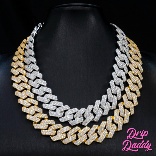 Close-up of Drip Daddy’s The Power Link Cuban chains in 20–27mm, with alternating white gold plated and yellow gold plated moissanite finishes, layered on a matte black bust. The Drip Daddy logo in pink is visible in the bottom right corner.