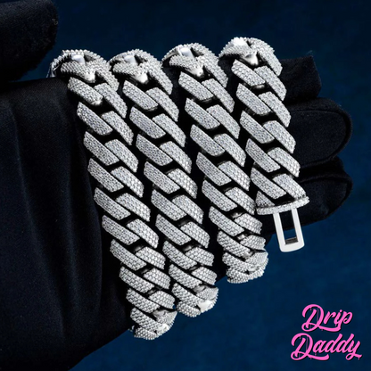 Close-up of multiple Drip Daddy’s The Power Link Cuban chains in 20–27mm white gold plated with moissanite stones, laid across a black gloved hand for display. The Drip Daddy logo in pink is visible in the bottom right corner.