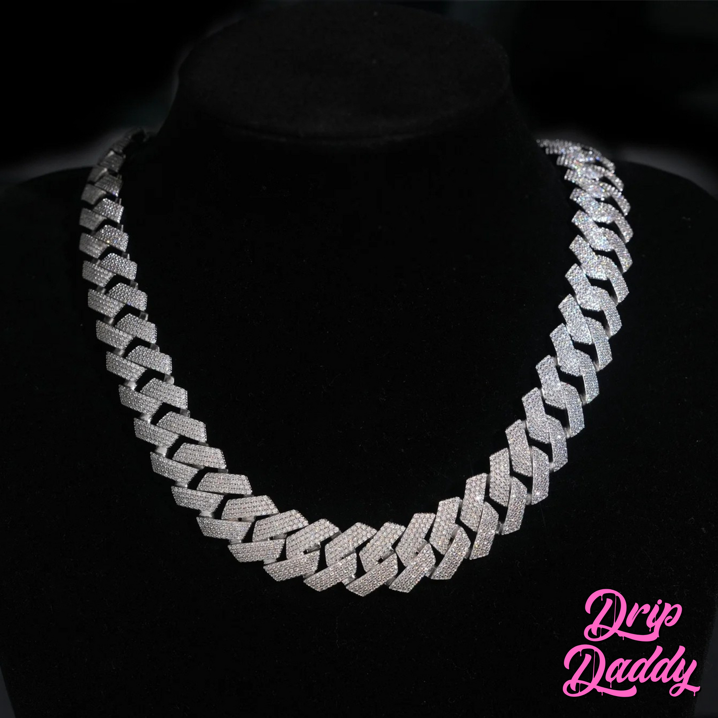 Close-up of Drip Daddy’s The Power Link Cuban chain in 20–27mm white gold plated with moissanite stones, displayed on a black velvet bust. The Drip Daddy logo in pink is visible in the bottom right corner.