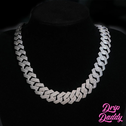 Close-up of Drip Daddy’s The Power Link Cuban chain in 20–27mm white gold plated with moissanite stones, displayed on a black velvet bust. The Drip Daddy logo in pink is visible in the bottom right corner.