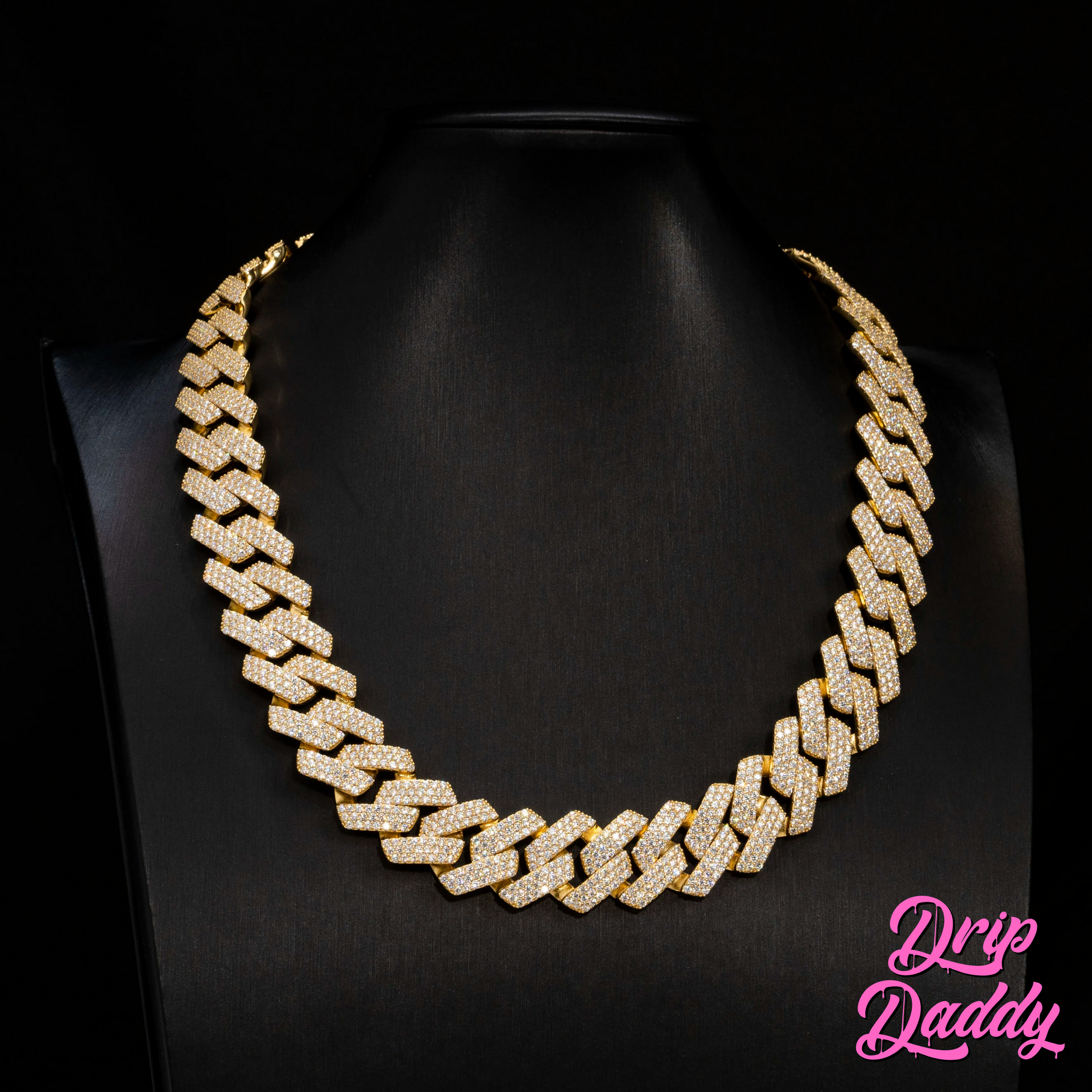 Close-up of Drip Daddy’s The Power Link Cuban chain in 20–27mm yellow gold plated with moissanite stones, displayed on a matte black bust. The Drip Daddy logo in pink is visible in the bottom right corner.