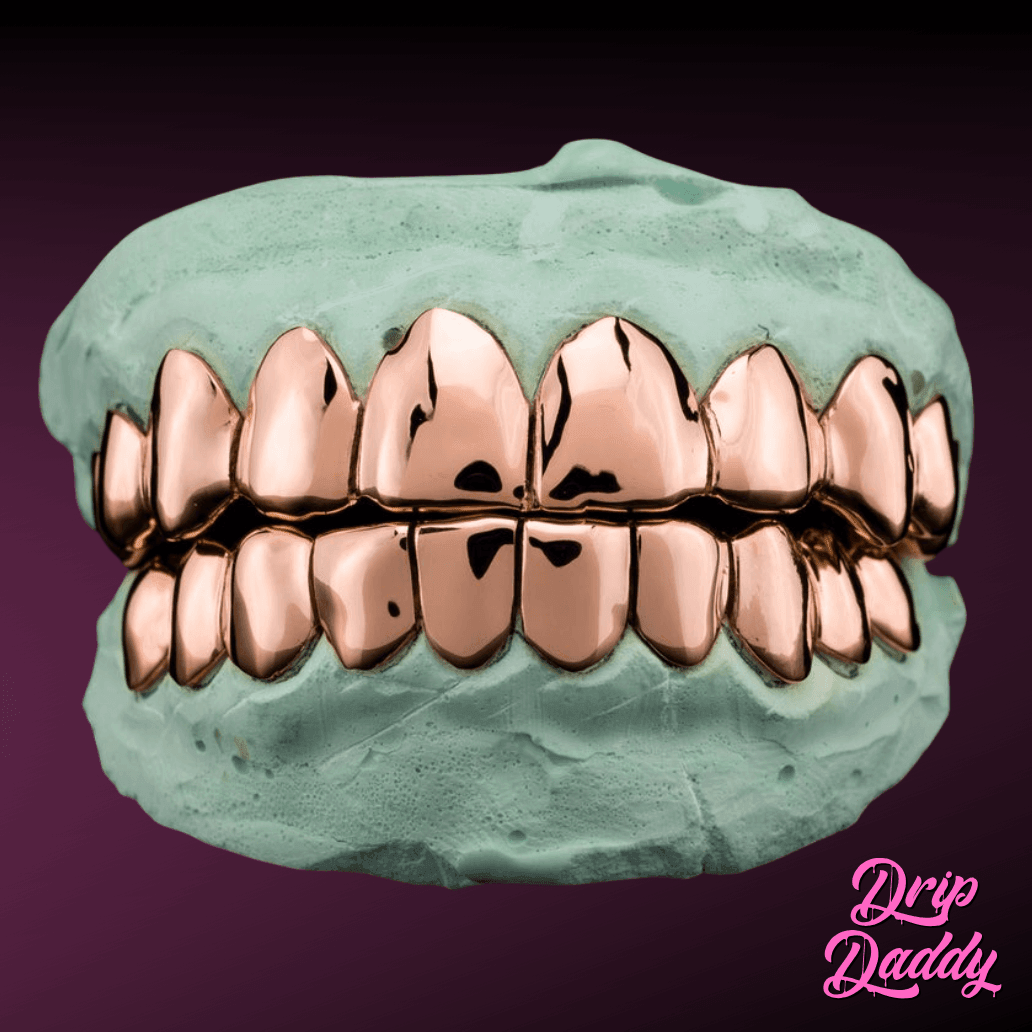 A gleaming set of rose gold–plated Solid Plain Grillz sits in a green dental mold, displayed on a deep purple background. The Drip Daddy logo is visible in pink cursive at the bottom right.
