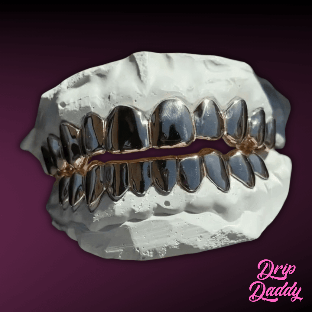 A white plaster dental mold presents Solid Plain Grillz featuring rhodium silver with rose gold accents. The metallic shine contrasts against the deep purple background, with the Drip Daddy logo in pink cursive at the bottom right.