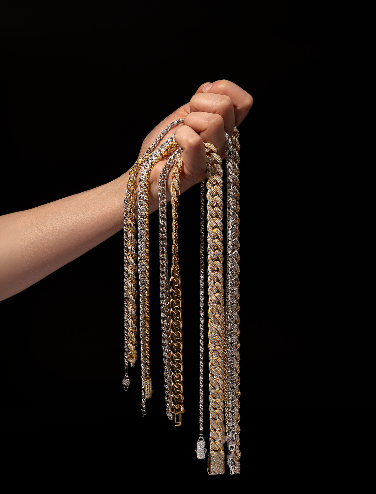 Hand holding multiple iced out Cuban link chains in gold and silver – premium hip hop jewelry by Drip Daddy.
