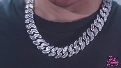 A rotating showcase of Drip Daddy’s Enforcer – 20mm Mixed-Cut Cuban Link Chain in white gold plating. The video highlights alternating emerald-cut and round moissanite stones set across the chain, with light reflections emphasizing the sparkle. The Drip Daddy logo appears in pink at the bottom right corner throughout the clip.